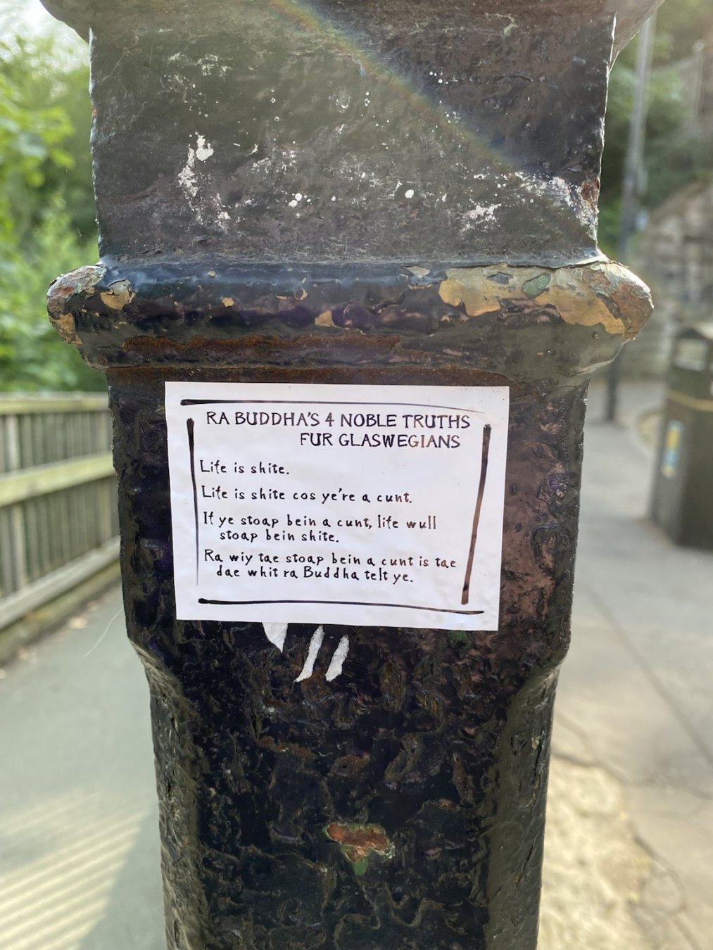 Sticker in a city park with the Buddhist 4 Noble Truths rendered in Glaswegian Scots